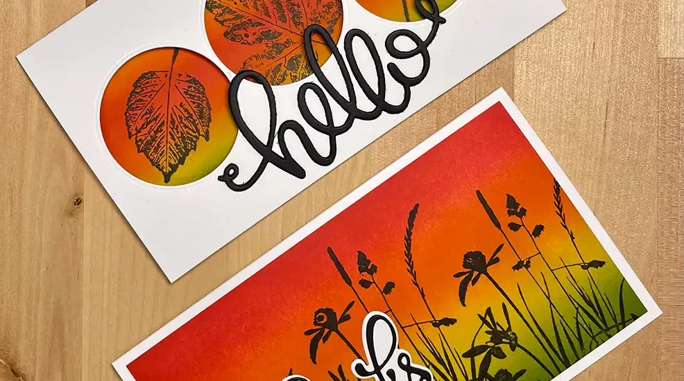 Two greeting cards on a wooden surface. The top card features the word "hello" with leaf designs, while the bottom card says "thanks" with silhouettes of grass and wildflowers against a sunset background. Perfect for quick crafts or DIY enthusiasts, these Rainbow Cards add a touch of charm to any occasion.