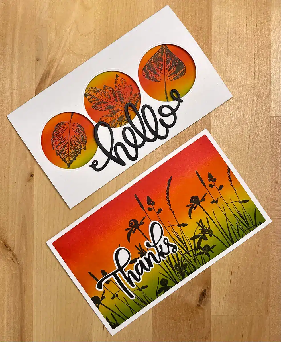 Two greeting cards on a wooden surface. The top card features the word "hello" with leaf designs, while the bottom card says "thanks" with silhouettes of grass and wildflowers against a sunset background. Perfect for quick crafts or DIY enthusiasts, these Rainbow Cards add a touch of charm to any occasion.