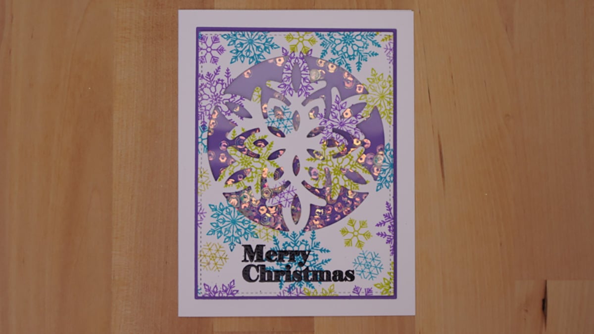 A Christmas card with a purple, green, and blue snowflake design that features a unique Snowflake Shaker element and the text "Merry Christmas" at the bottom.