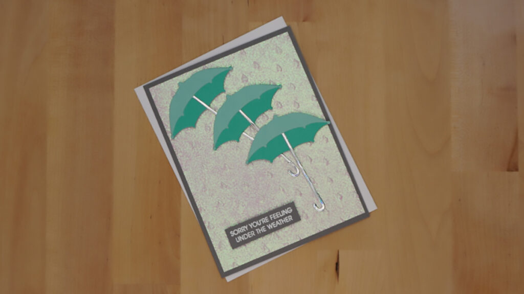 The third of 4 cards made with products from Spellbinders' January holds three teal umbrellas over a glittery raindrop background