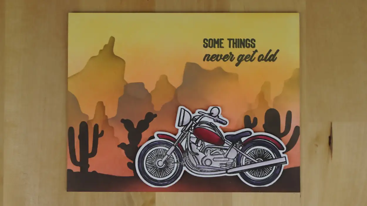 This is a photo of a motorcycle on a anniversary card. And it's perched in front of a beautiful dessert sunset.