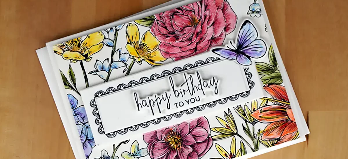 A BetterPress birthday card with "happy birthday to you" text, adorned with colorful floral and butterfly illustrations, placed on a wooden surface.