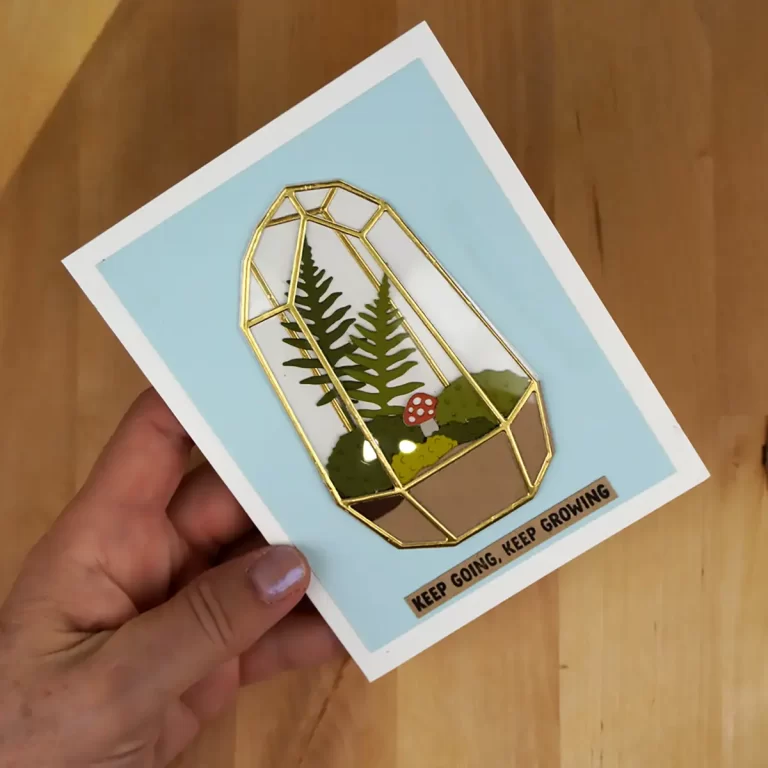 Hand holding a greeting card with a geometric terrarium illustration featuring plants and a mushroom. Text at the bottom reads "KEEP GOING. KEEP GROWING." Ideal for cardmaking enthusiasts or to inspire campers at summer camp.