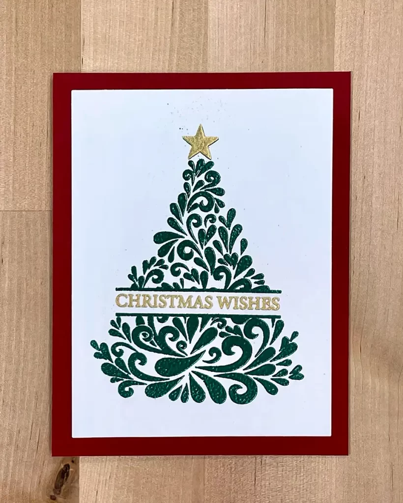 A beautifully crafted Christmas card featuring a green, ornate tree design with a gold star on top. "CHRISTMAS WISHES" is elegantly written in gold text across the tree, enhanced with heat embossing. The card is framed with a red border, perfect for festive greetings.