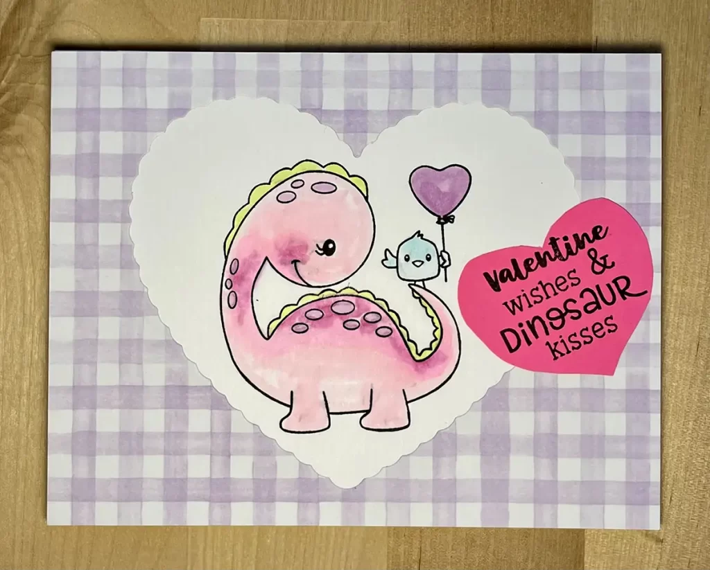 Cute valentine card with purple gingham and a dinosaur and bird colored with alcohol markers. 