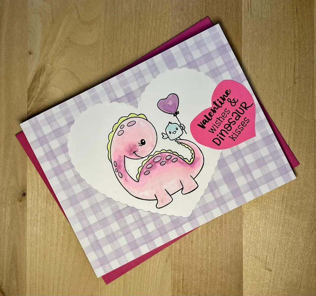 Cute valentine card with purple gingham and a dinosaur and bird colored with alcohol markers. 