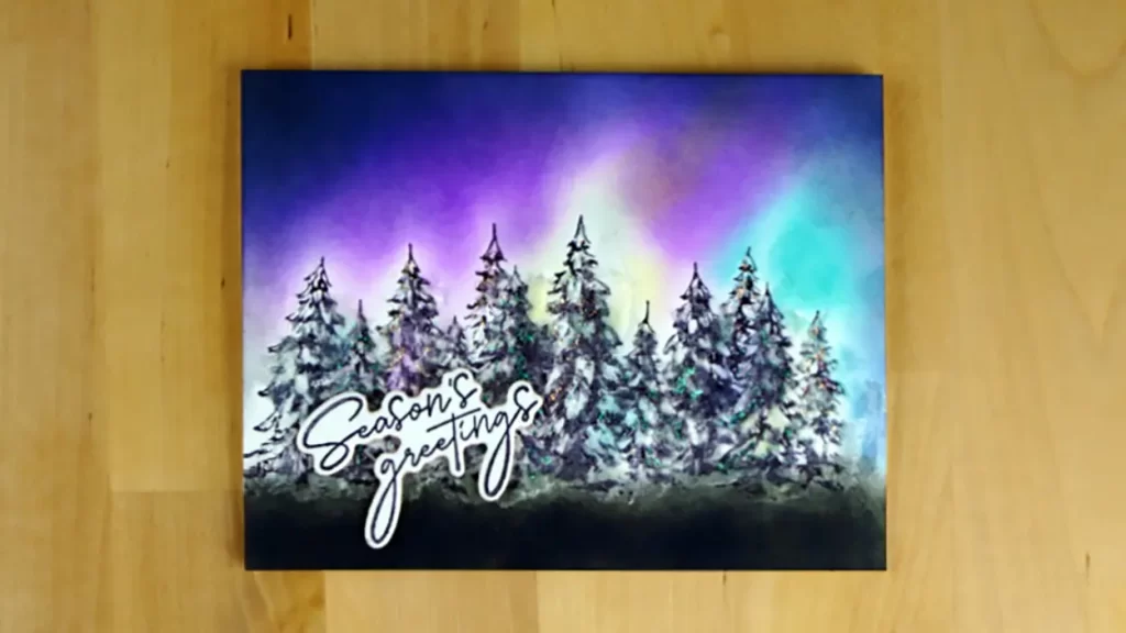 A holiday card featuring the new Spellbinders' Betterpress plate, Season's Greetings Evergreens.  And, the card is colored to represent northern lights behind the trees.