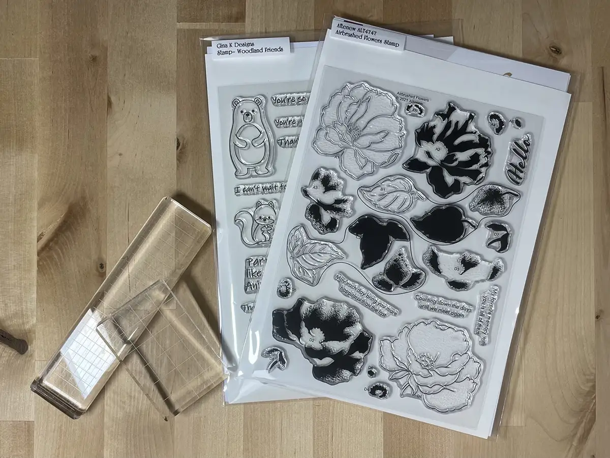 Two sets of clear stamps featuring nature-themed designs, along with an acrylic stamping block, are arranged on a wooden surface—perfect for building your cardmaking startup tool kit.
