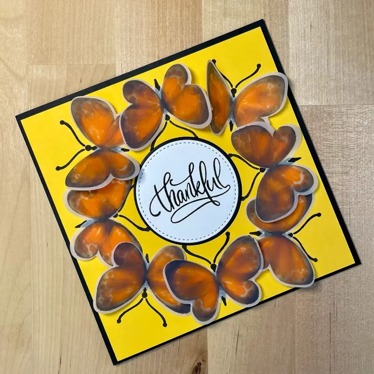A handmade card with vibrant orange butterflies surrounding a central circle with the handwritten word "Thankful" on a yellow background, showcasing beautiful cardmaking techniques.
