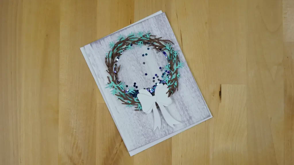 A pretty shaker card created using Spellbinders' new Build-A-Wreath Die Set.  The Wreath is in mocha and teal and has a white ribbon. 