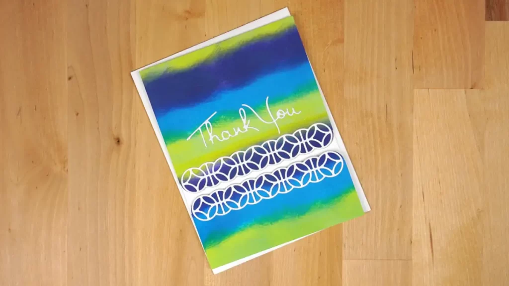 A blue and green thank you card on a wooden floor.