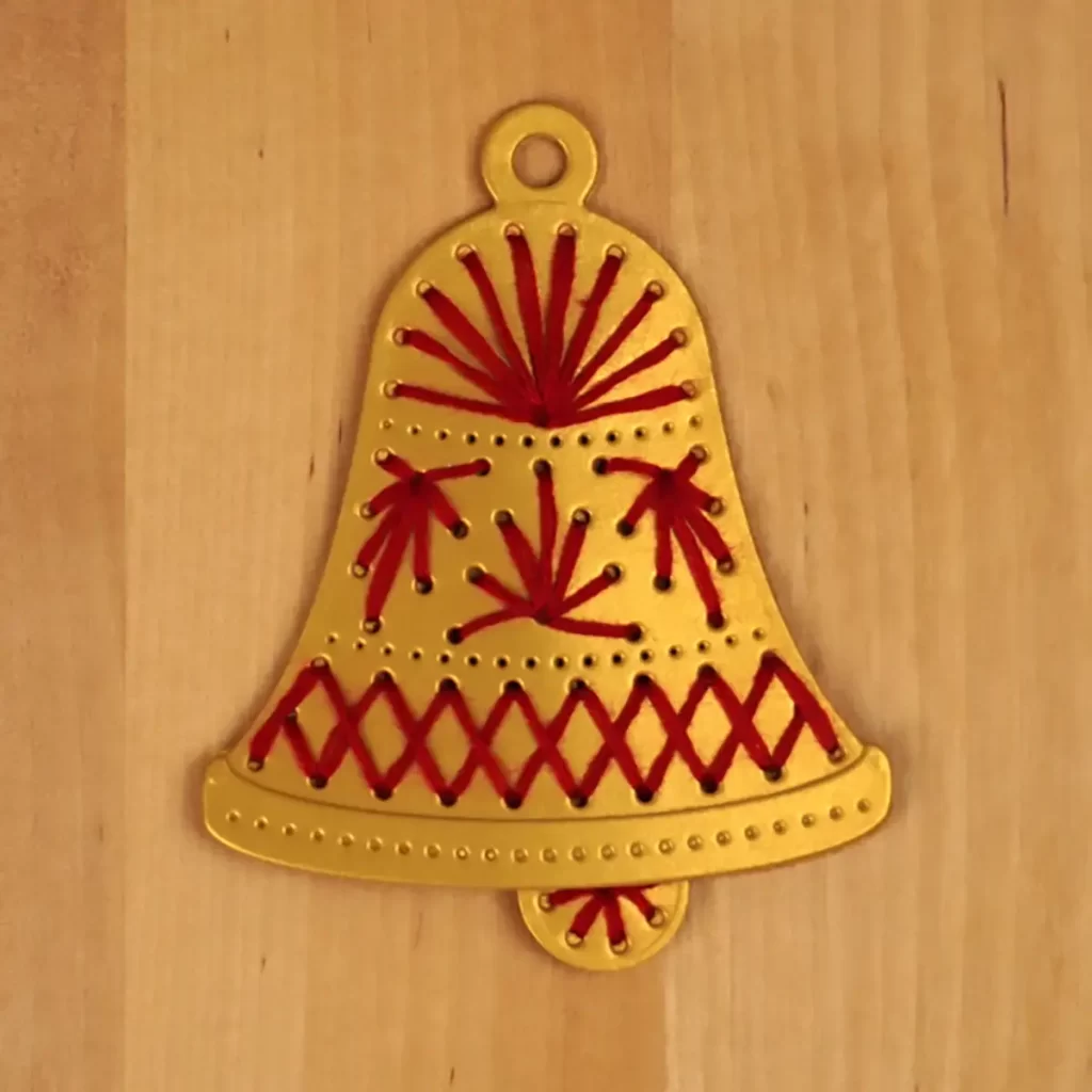 A gold bell ornament that hangs on the Stitchmas Christmas Tree card
