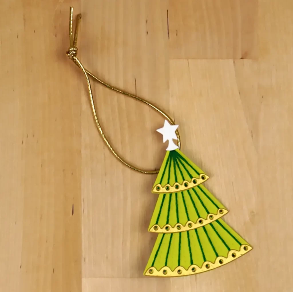 A green christmas tree ornament hanging on a wooden surface.