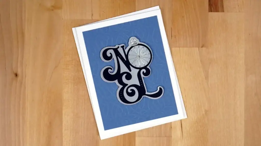 A blue stitched noel card featuring an ornament for the letter "O".