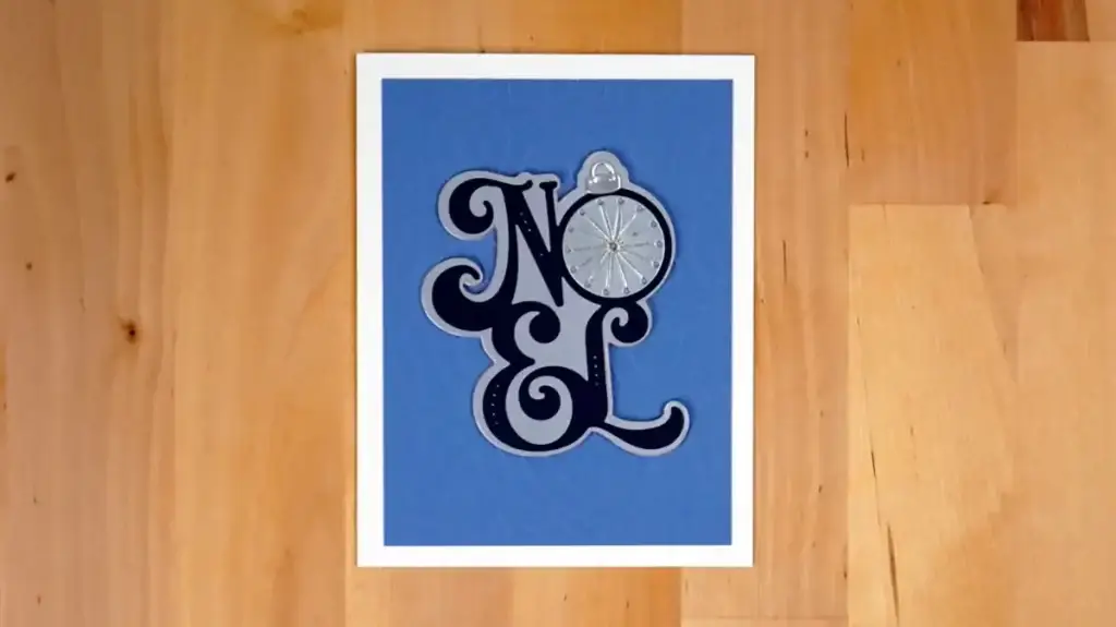 A blue stitched noel card featuring an ornament for the letter "O".