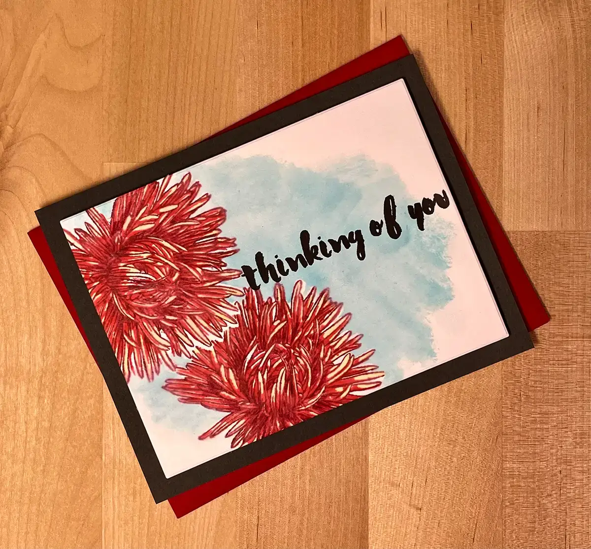 Using masking methods, a card is beautifully designed with red flowers and the heartfelt words "thinking of you.