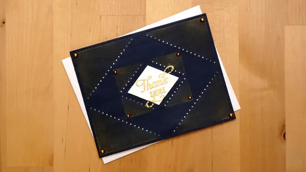 A blue and gold thank you card with stitching on a wooden floor.