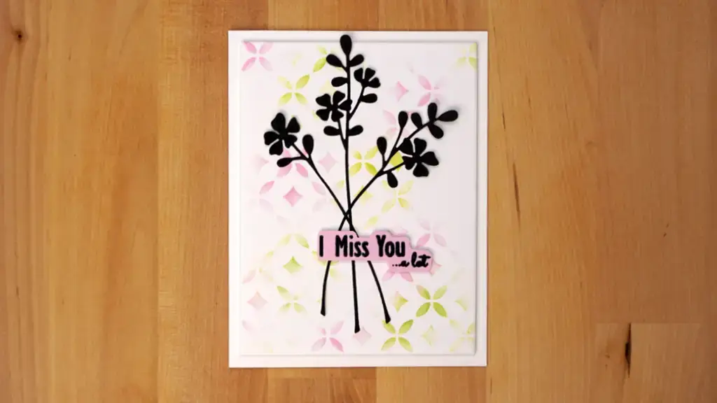 A card with black flowers and foil accents on a wood surface.