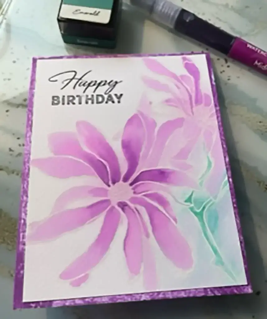 A birthday card featuring purple flowers intricately painted using the watercolor technique.