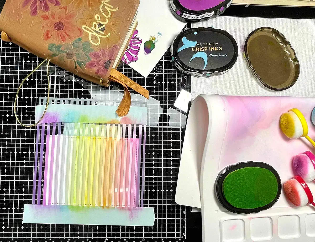A group of art supplies, including crafters and a travel's notebook, on a table.