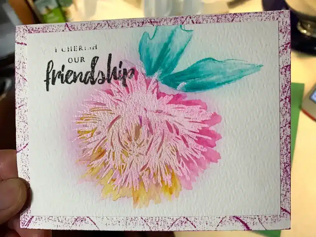 A hand holding a watercolor card with a flower on it, showcasing one of the 4 ways to watercolor.