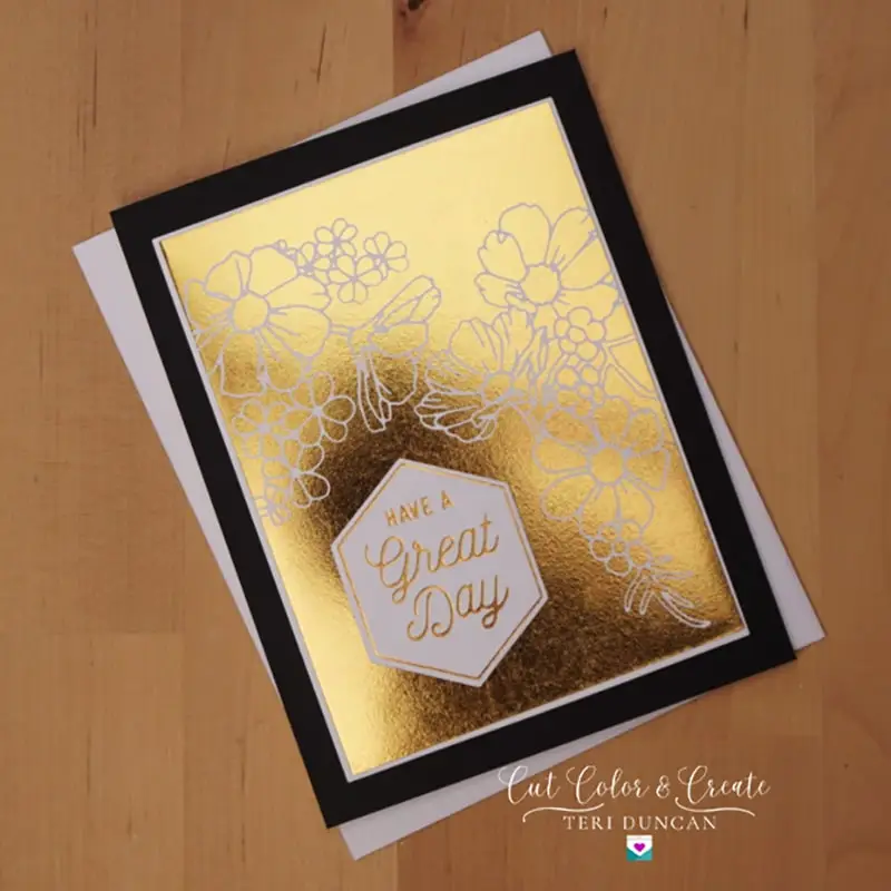 A greeting card with a golden floral design and the text "Great Day" in the center. The card is layered on black and white cardstock, set against a wooden background.