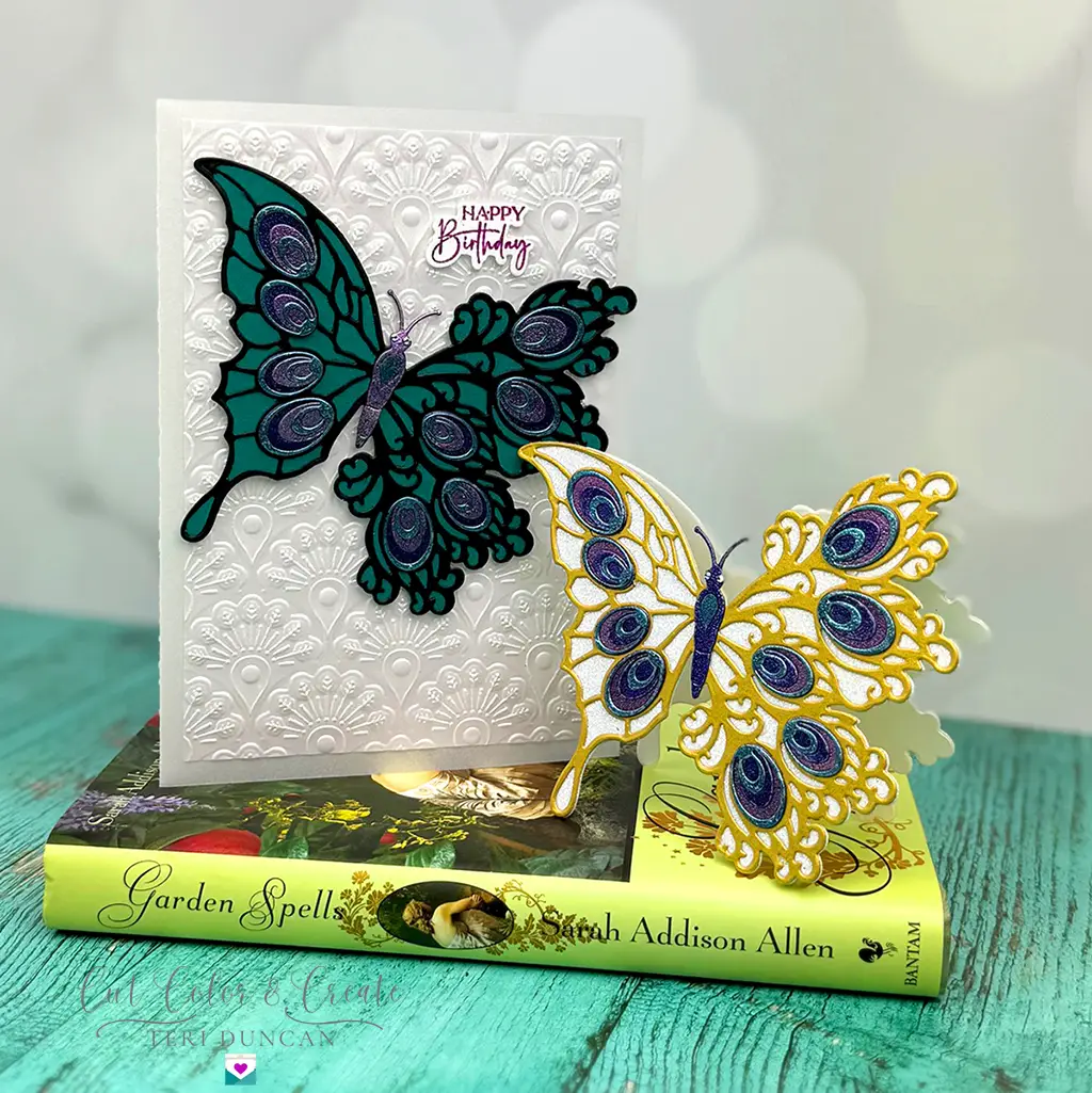 Lovely pair of cards featuring the Peacock Butterfly: one in purples and teals flying over a lacy peacock background and the other glittery white and gold with purple and teal accents cut to the the shape of the butterfly.