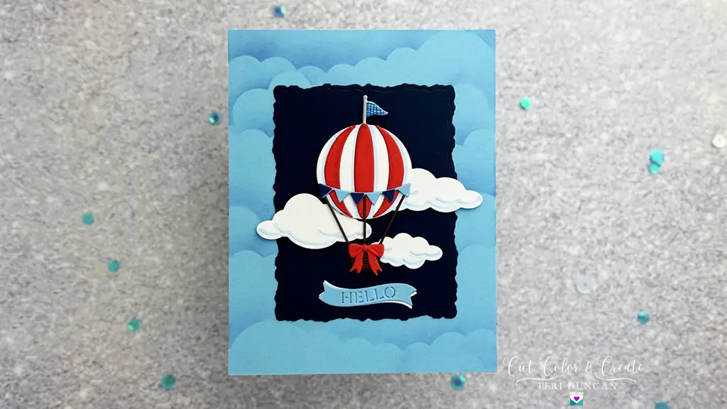 A greeting card features a red and white striped hot air balloon floating among clouds on a blue background, reminiscent of the excitement of Advent countdowns. The word "HELLO" is prominently displayed on a blue banner at the bottom, making it perfect for a festive Day 1 surprise.