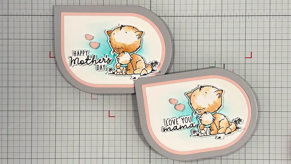Two teardrop-shaped greeting cards featuring a kitten—one says "Happy Mother's Day," the other "Love You Mama"—are displayed on a grid-patterned surface.