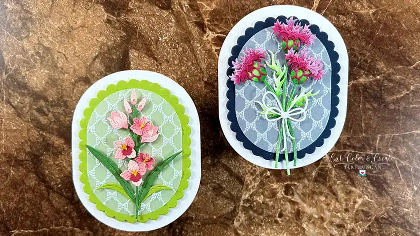 Two oval-shaped handmade Wildflower cards with quilled flowers on lace-patterned backgrounds, one with pink blossoms on green, the other with purple blooms tied with a white bow on grey—a perfect way to make greeting cards truly unique.