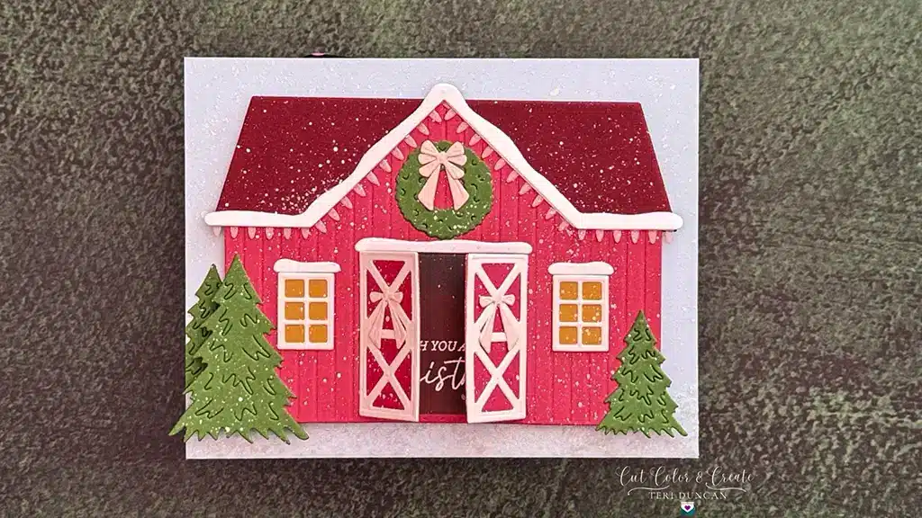 A festive Country Christmas Barn card features a red barn with a wreath above the doors, flanked by two green trees, perfect for Holiday Cardmaking against a textured background.