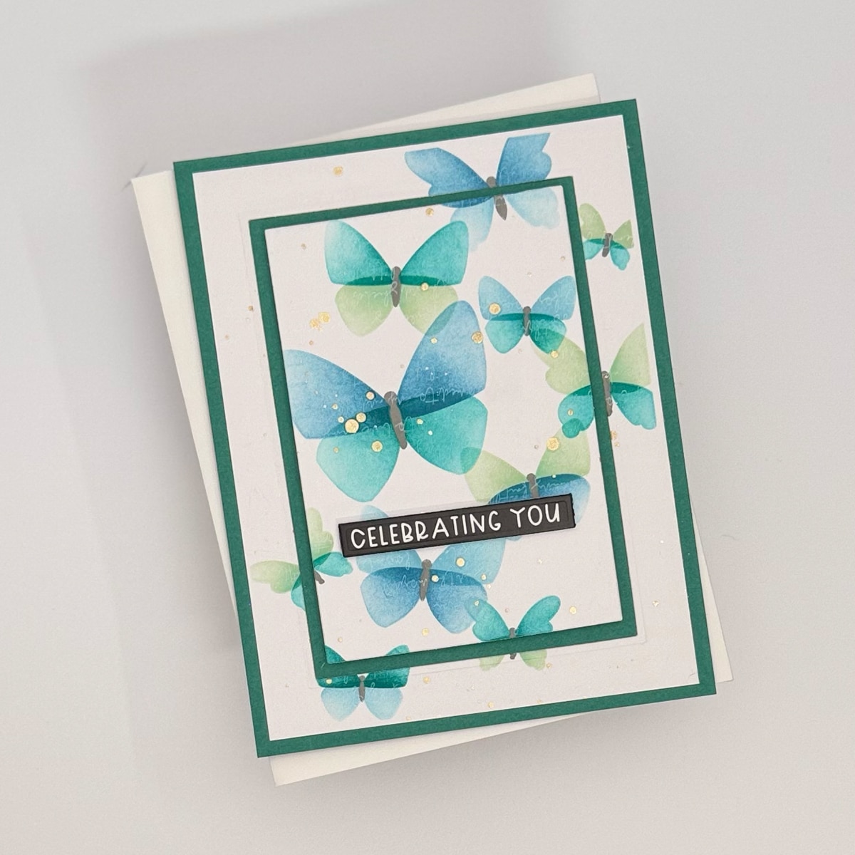 A set of 4 handmade cards with a teal border, decorated with blue and green watercolor butterflies that flit & flitter around the text "CELEBRATING YOU" in the center.