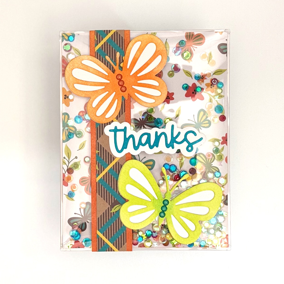 A vibrant Handmade Card featuring orange and yellow butterflies, colorful sequins, a patterned strip, and "thanks" in blue letters on a white background—a cheerful Thanks Butterfly Shaker Card for any occasion.