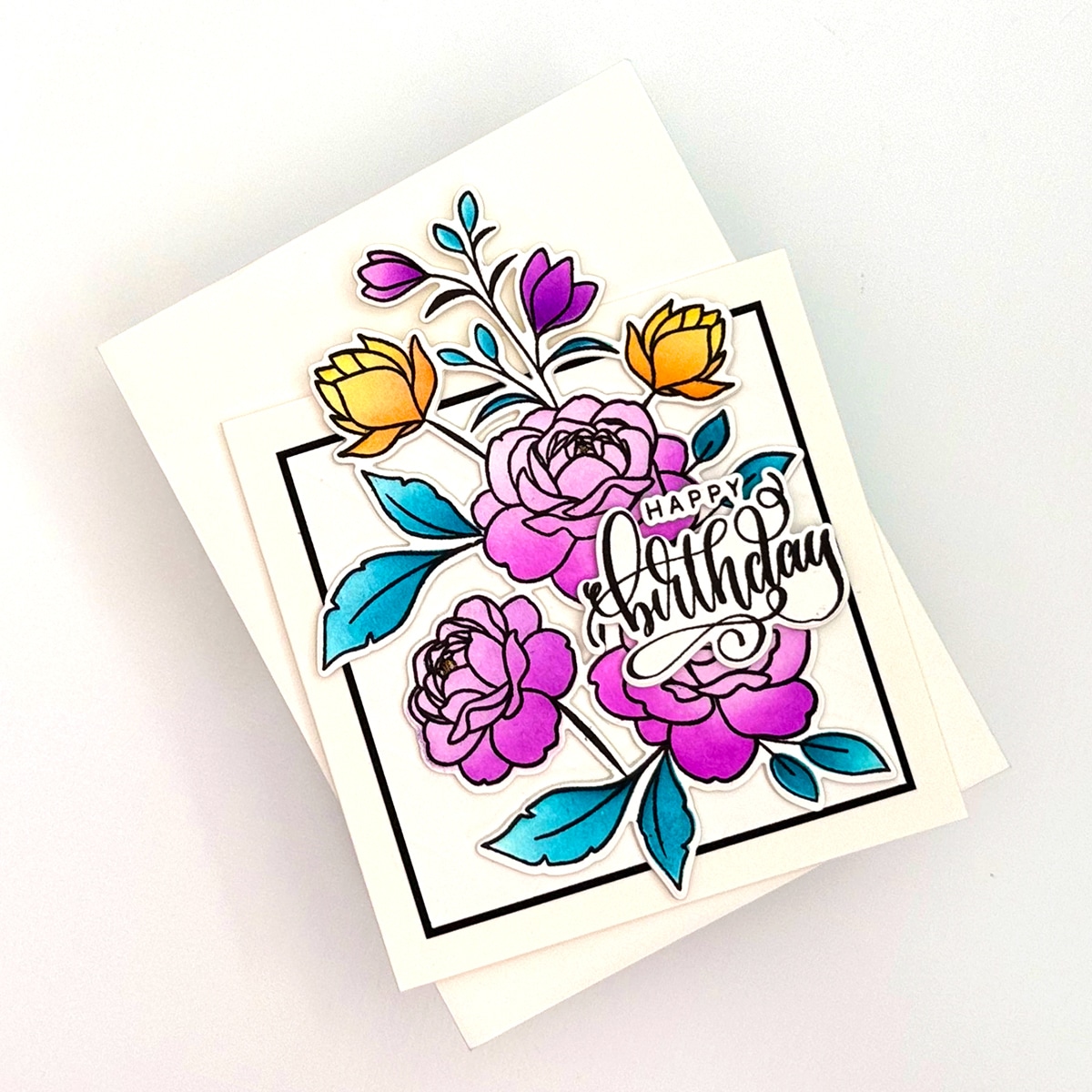A handmade Off the Edge Birthday card featuring colorful flowers with purple and yellow petals, blue leaves, and the words "Happy Birthday" in decorative script.