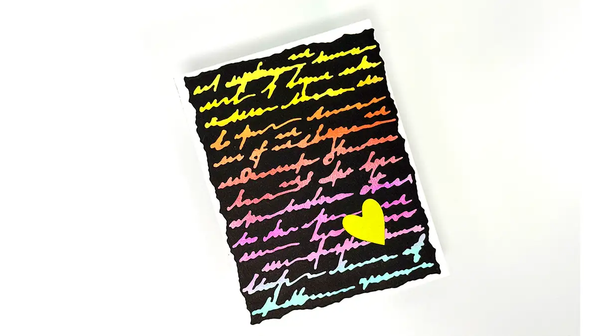 A piece of paper with colorful cursive writing reading "Beautifully Imperfect" on a black background and a yellow heart shape at the bottom right, set against a white surface—a charming addition to any Greeting Cards Set.