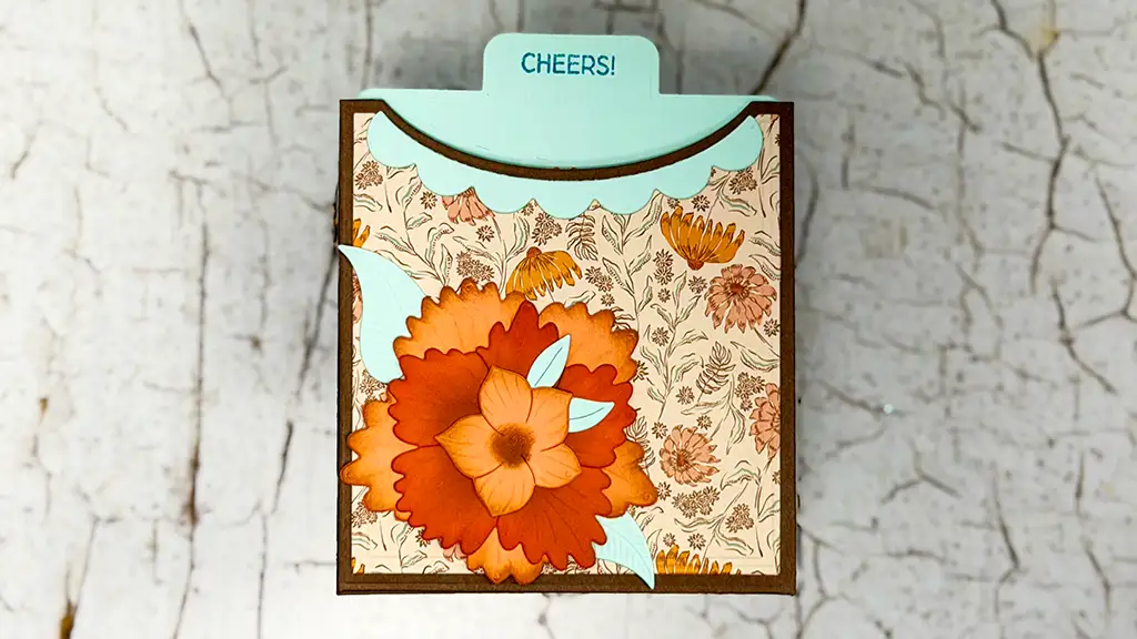 A decorative card with a “CHEERS!” tab, featuring orange floral patterns and leaves on a textured background—perfect for card making or adding flair to fun die cut birthday cards.