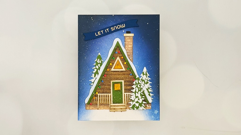 A cozy holiday scene card featuring a snow-covered cabin adorned with colorful lights, two pine trees, and a "LET IT SNOW" banner set against a blue snowy background—perfect for capturing the charm of a ski lodge getaway.