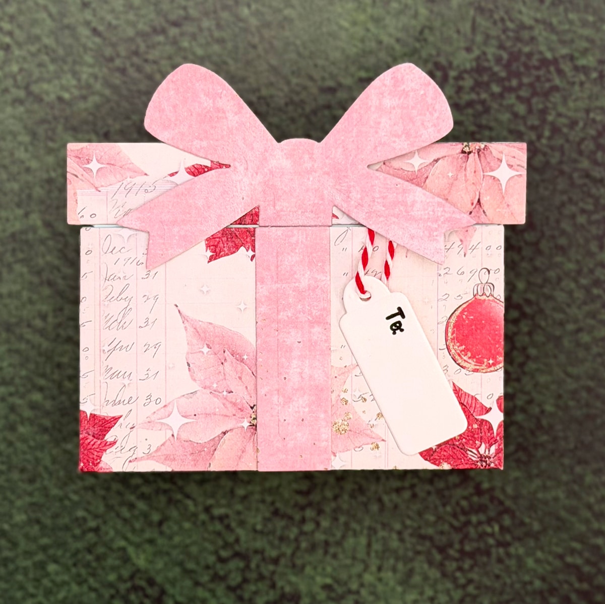 A rectangular gift box with pink floral wrapping paper, a large pink bow, and a white gift tag labeled "To:" makes a charming Christmas Gift Card Holder, set against a green textured background.