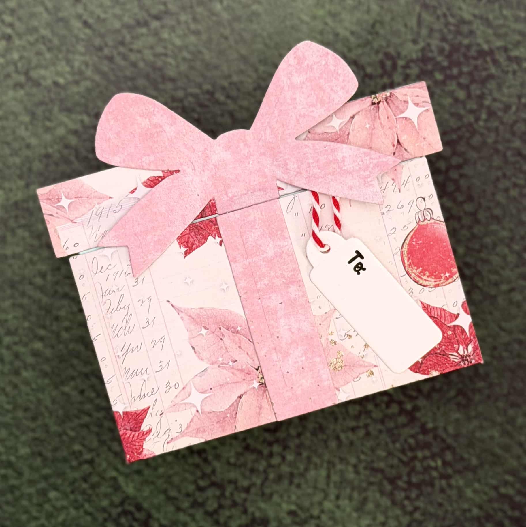 A Christmas Gift envelope shaped like a present, featuring pink poinsettia designs, a large pink bow, and a white "To:" tag on a green textured background—perfect as a festive Gift Card Holder.