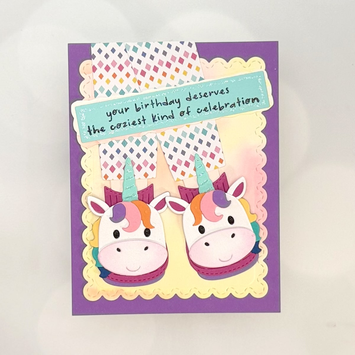 A Unicorn Birthday Card featuring two cartoon unicorn slippers and a sign that reads, "your birthday deserves the coziest kind of celebration," set against a playful purple and yellow background.